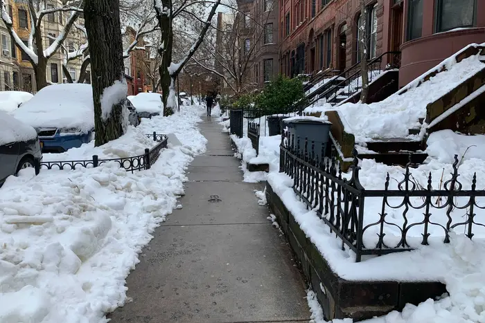 A cleared sidewalk on a street of brownstones